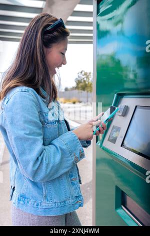 Jeune femme achetant un billet pour les transports en commun en machine automatique. Vertical Banque D'Images