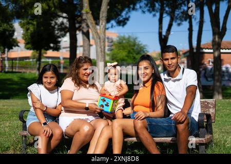 Portrait de famille péruvienne de jeune père, mère, tante, grand-mère et bébé assis sur un banc de parc. Famille latine Banque D'Images