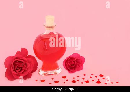 Cadeau amoureux pour la Saint-Valentin avec fleur de rose, bouteille de parfum en forme de coeur, confettis de coeur rouge dispersé sur fond rose. Concept d'amour romantique. Banque D'Images