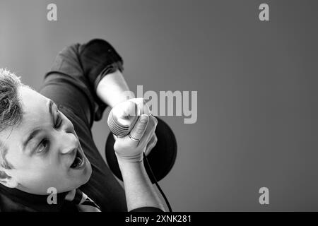 Jeune homme vêtu d'une tenue formelle chante passionnément dans un microphone vintage, capturé dans un portrait monochrome dynamique Banque D'Images