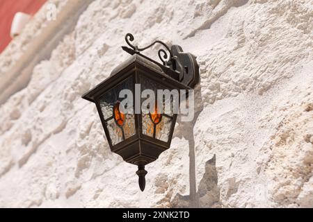 Lampe suspendue à un mur dans la vieille ville. Mur avec un lampadaire monté dessus, créant un effet d'éclairage doux Banque D'Images