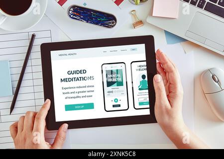 Mains utilisant une tablette avec une application de méditation à l'écran, placées sur un bureau d'affaires. Vue de dessus. Banque D'Images