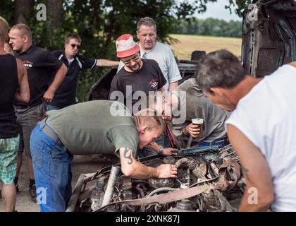 Groupe d'hommes travaillant en collaboration sur un moteur de voiture lors d'un derby de démolition, symbolisant le travail d'équipe et la résolution de problèmes. Banque D'Images