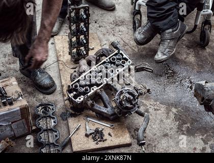 Mécaniciens bricolant méticuleusement avec un moteur de voiture démonté dans un atelier, symbolisant la précision et le travail d'équipe. Banque D'Images