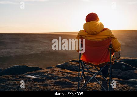 Une femme dans une veste jaune se relaxant seule au sommet de la montagne au lever ou au coucher du soleil le jour froid du printemps. Concept Travel Lifestyle Banque D'Images