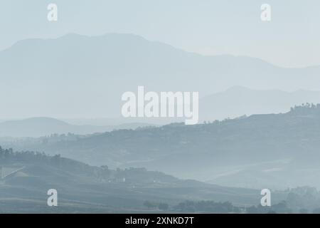 TEMECULA, Californie, États-Unis — les basses montagnes entourant Temecula Valley sont silhouettées contre la ligne d'horizon dans la lumière du petit matin. Haze adoucit les contours des collines lointaines, créant un effet de couches caractéristique du paysage de Californie du Sud dans cette région viticole. Banque D'Images