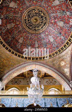 ISTANBUL, Turquie / Türkiye — le plafond en forme de dôme dans l'opulente salle du trône impérial dans le harem du palais de Topkapi, Istanbul. Cette chambre richement décorée, ornée de carreaux Iznik complexes, d'ornements dorés et de riches meubles, servait de salle d'audience privée pour le sultan ottoman dans les limites isolées du harem impérial. La salle reflète la maîtrise artistique et le luxe de l'architecture impériale ottomane, offrant un aperçu du monde de la cour ottomane. Banque D'Images