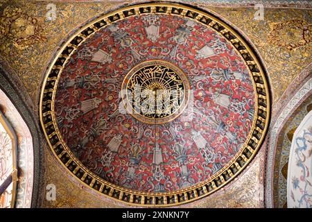 ISTANBUL, Turquie / Türkiye — le plafond en forme de dôme dans l'opulente salle du trône impérial dans le harem du palais de Topkapi, Istanbul. Cette chambre richement décorée, ornée de carreaux Iznik complexes, d'ornements dorés et de riches meubles, servait de salle d'audience privée pour le sultan ottoman dans les limites isolées du harem impérial. La salle reflète la maîtrise artistique et le luxe de l'architecture impériale ottomane, offrant un aperçu du monde de la cour ottomane. Banque D'Images