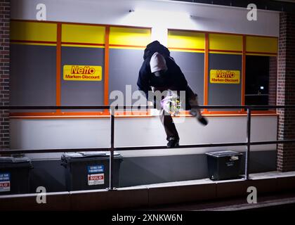 Jeune homme activement engagé dans la plongée dans des bennes à ordures pour la nourriture comestible à l'extérieur d'un supermarché Netto discount la nuit à Berlin, en Allemagne. Banque D'Images