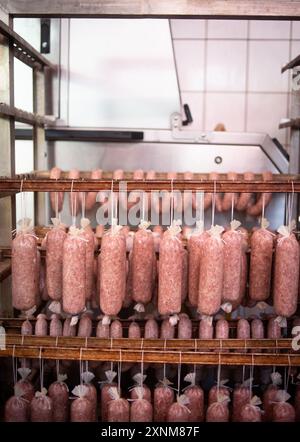 Rangées de saucisses de viande biologiques suspendues dans une usine pendant la phase de transformation. Lignes de production industrielle assurant la qualité et l'hygiène dans la fabrication d'aliments biologiques. Banque D'Images