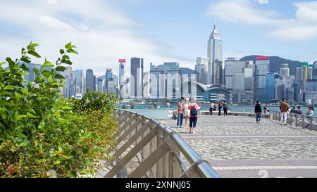 Horizon de Hong Kong par une journée ensoleillée avec des touristes marchant le long de la promenade. Hong Kong - 29 mai 2024 Banque D'Images