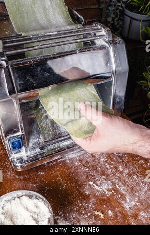 Les mains adultes préparent des pâtes maison, en roulant la pâte avec une machine à pâtes dans une cuisine de restaurant. Banque D'Images