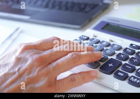 La main d'une consultante plus âgée faisant des calculs sur une calculatrice dans son bureau Banque D'Images