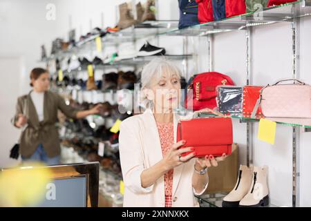 Dans la salle d'exposition de maroquinerie, la femme senior regarde le sac à main miniature rouge Banque D'Images