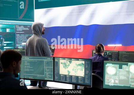 Un hacker travaillant dans un espace de travail INFORMATIQUE gouvernemental avec le drapeau américain sur grand écran. Assurer la cybersécurité, l’analyse des cybermenaces et la surveillance mondiale pour assurer la cyberprotection. Banque D'Images