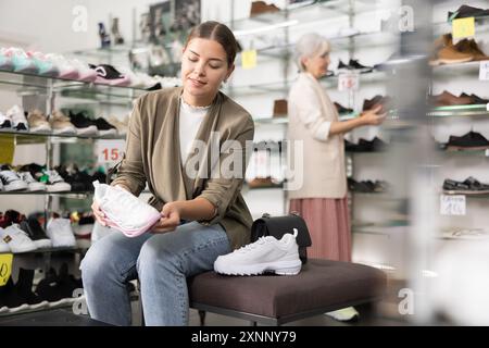 Dans le magasin de chaussures, une femme s'assoit sur un pouf et essaie des baskets Banque D'Images