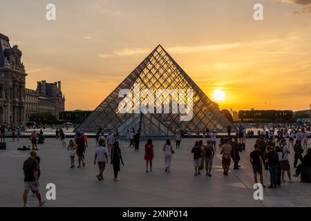 Paris, France - 29 juillet 2024 : coucher de soleil vibrant sur la pyramide de verre du Louvre avec foule en soirée Banque D'Images