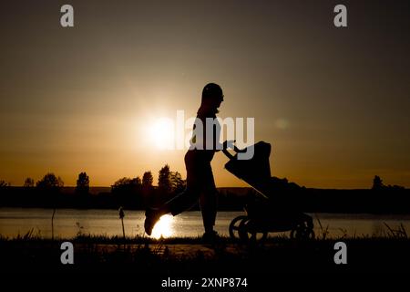 Silhouette d'une mère tirant une poussette contre le coucher du soleil près du lac Banque D'Images