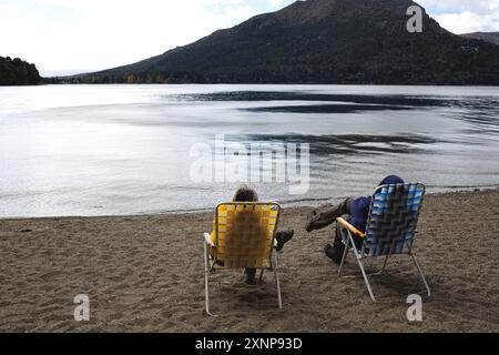 Deux personnes se détendent sur une plage tranquille au bord du lac, en profitant de la vue panoramique sur la montagne Banque D'Images