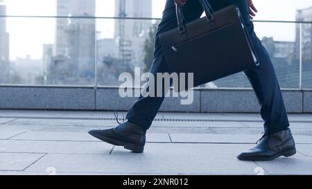 Image recadrée de partenaires d'affaires exerçant son porte-documents sur l'avant-plan alors que leur collègue debout sur l'arrière-plan Banque D'Images