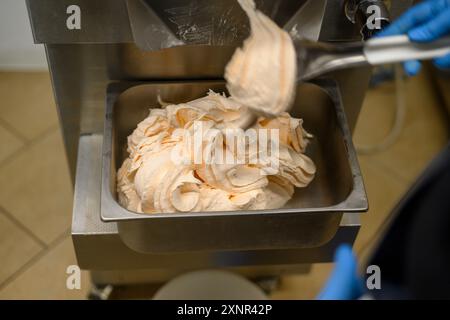 Une vue rapprochée de gelato fraîchement préparé prélevé dans un récipient métallique. La glace a une texture crémeuse et une couleur orange clair, indiquant un fr Banque D'Images