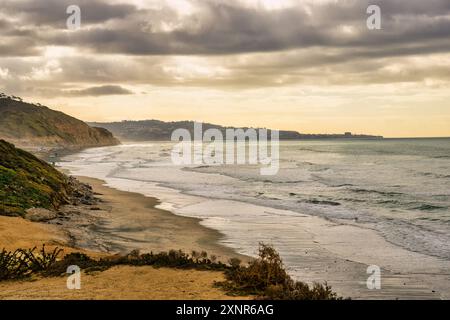 Paysage côtier pittoresque au coucher du soleil avec des vagues qui s'écrasent sur la plage et des falaises en arrière-plan à la plage d'État Torrey Pines Banque D'Images