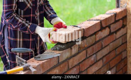 Une jeune maçon femelle construit un mur, met une brique sur un mortier de ciment Banque D'Images