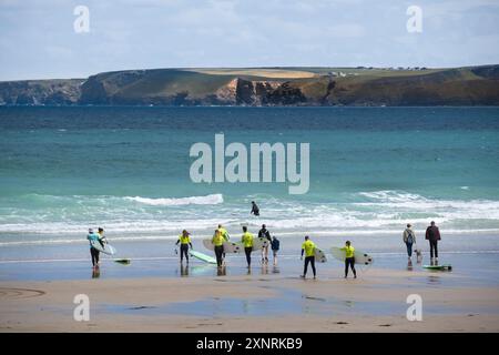 Un instructeur de surf de Escape Surf School et un groupe de novices de surf marchant dans la mer pour une leçon de surf sur Towan Beach à Newquay à Cornwa Banque D'Images