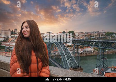 Femme en Veste orange avec Dom Luis I Bridge et Porto Cityscape au coucher du soleil Banque D'Images