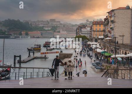 Promenade animée au bord de la rivière au coucher du soleil à Porto, Portugal avec bâtiments historiques Banque D'Images