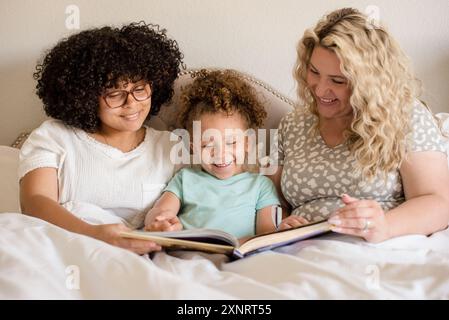 Mère et deux filles lisant le livre dans le lit avec tous smilinga Banque D'Images