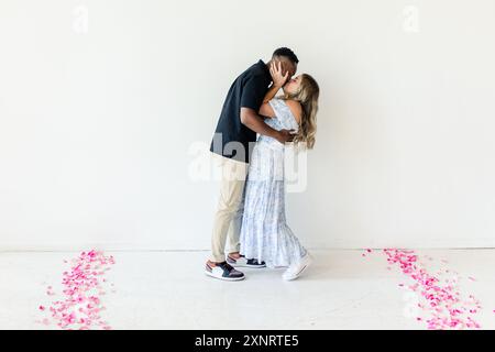 Couple embrassant dans une pièce avec des pétales de fleurs roses sur le sol Banque D'Images