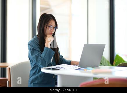 Une femme est assise à un bureau avec un ordinateur portable ouvert devant elle Banque D'Images