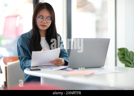 Une femme est assise à une table avec un ordinateur portable et une pile de papiers Banque D'Images