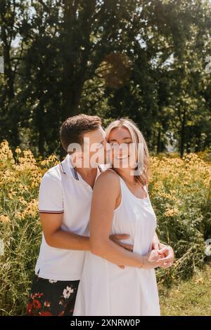Jeune couple embrassant et souriant devant des fleurs sauvages Banque D'Images