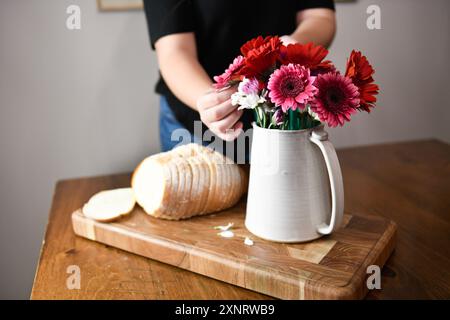 Personne arrangeant des fleurs lumineuses dans un vase à côté d'un pain tranché Banque D'Images