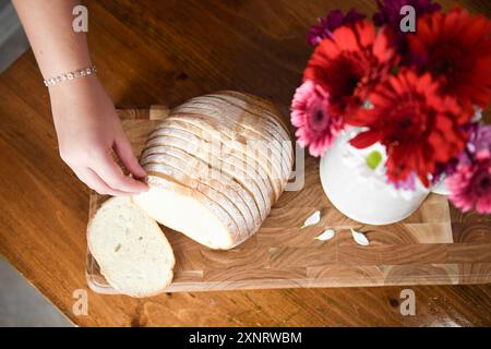 Main tendue pour une tranche de pain à côté d'un vase de fleurs sur Banque D'Images