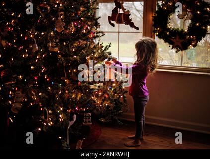 Tout-petit décorant arbre de Noël coloré devant la fenêtre Banque D'Images