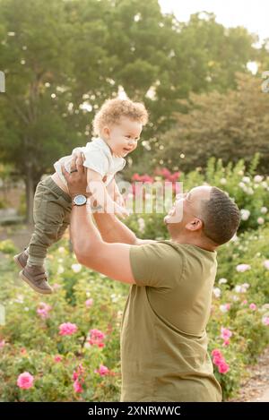 Père soulevant son fils dans l'air dans le jardin Banque D'Images