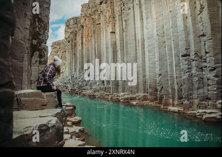 Femme assise sur des colonnes de basalte dans le canyon de Stuðlagil, Islande Banque D'Images