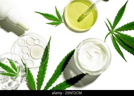 Huile de CBD en compte-gouttes, teinture de THC en tasses de laboratoire, crème cosmétique et sérum et feuilles de cannabis de chanvre isolées sur fond blanc. Soins biologiques de la peau Banque D'Images