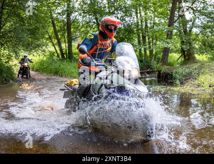 Motocycliste professionnel en équipement moto complet chevauchant un vélo enduro dans la nature, le conducteur roule à travers la boue et les flaques d'eau, course de moto. Tournam tout-terrain Banque D'Images