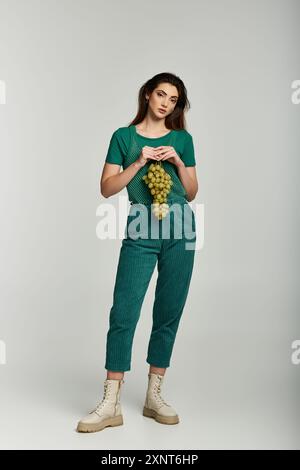 Une jeune femme dans une tenue verte tient un bouquet de raisins. Banque D'Images