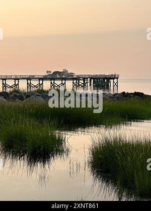 NORWALK, CY, USA- 28 JUILLET 2024 : la lumière paisible du matin illumine doucement les eaux calmes tandis qu'un quai s'étend dans la distance à Calf Pasture bea Banque D'Images