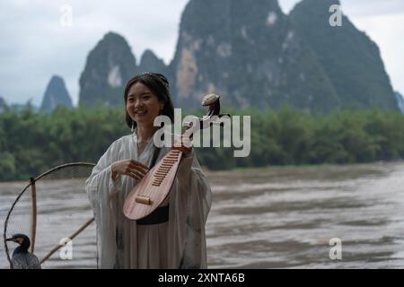 Hanfu Girl souriant au-dessus de Li River met un instrument traditionnel de pipa dans son dos Banque D'Images