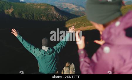 Un homme et une femme se tiennent debout au sommet d'une montagne majestueuse, leurs bras enroulés l'un autour de l'autre dans une étreinte chaleureuse, se fondant dans le vaste paysage impressionnant. Banque D'Images