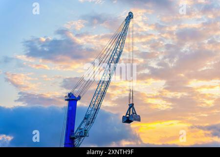 Grue industrielle imposante silhouette contre un ciel de coucher de soleil vibrant, mettant en vedette son bras mécanique et son seau, parfait pour la construction et l'industrie Banque D'Images