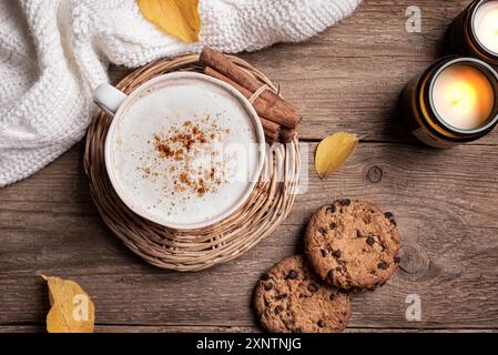 Composition confortable d'automne. Tasse de café cappuccino, biscuits aux pépites de chocolat, bougies allumées et feuilles jaunes d'automne sur fond en bois, vue de dessus. HY Banque D'Images