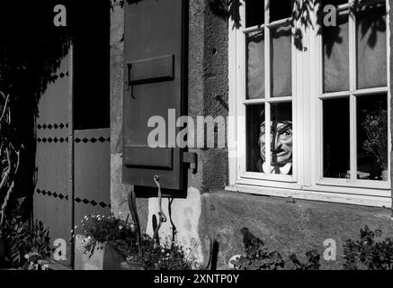 Mystérieuse poupée jetant un coup d'œil par une fenêtre. Image monochrome Banque D'Images