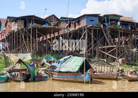 Maisons sur pilotis érigées au-dessus de l'eau avec des bateaux de pêche amarrés le long du rivage à Tonle SAP, au Cambodge, montrant un mode de vie traditionnel. Banque D'Images